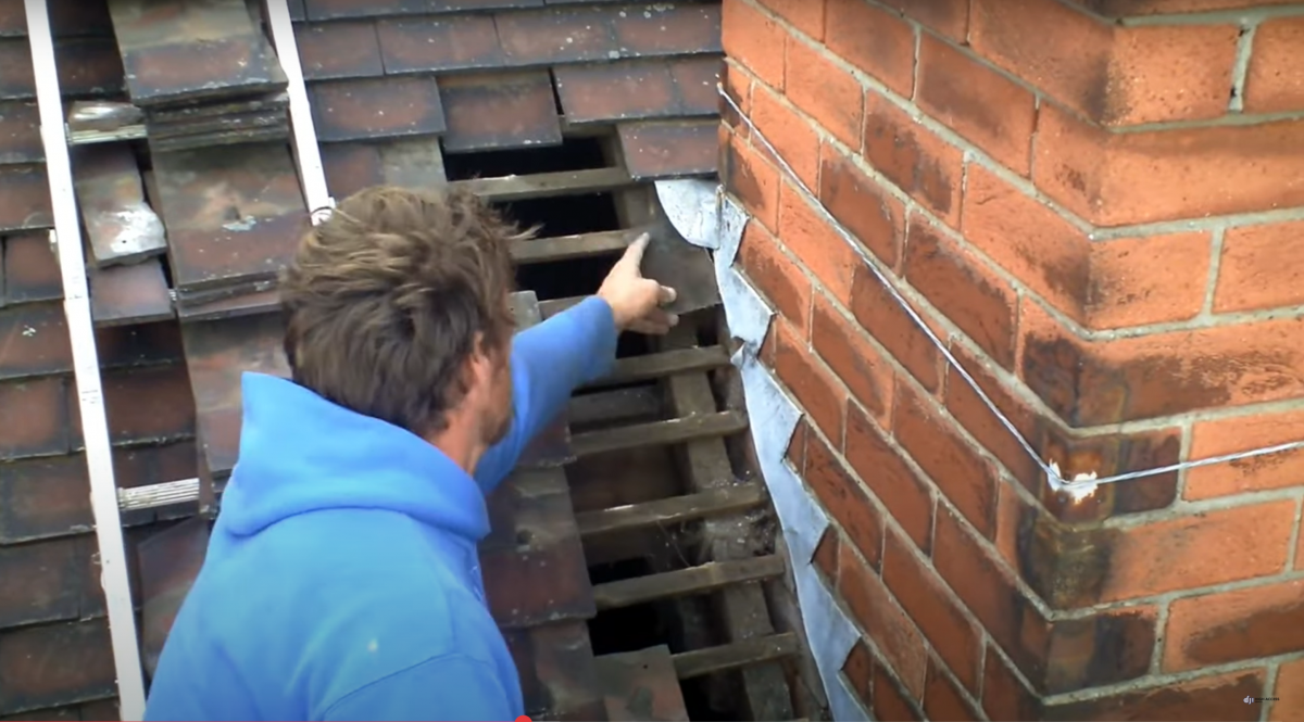 Danny Iwanejko sat on roof ladders next to a chimney in Sherwood, Nottingham repairing the chimney flashings
